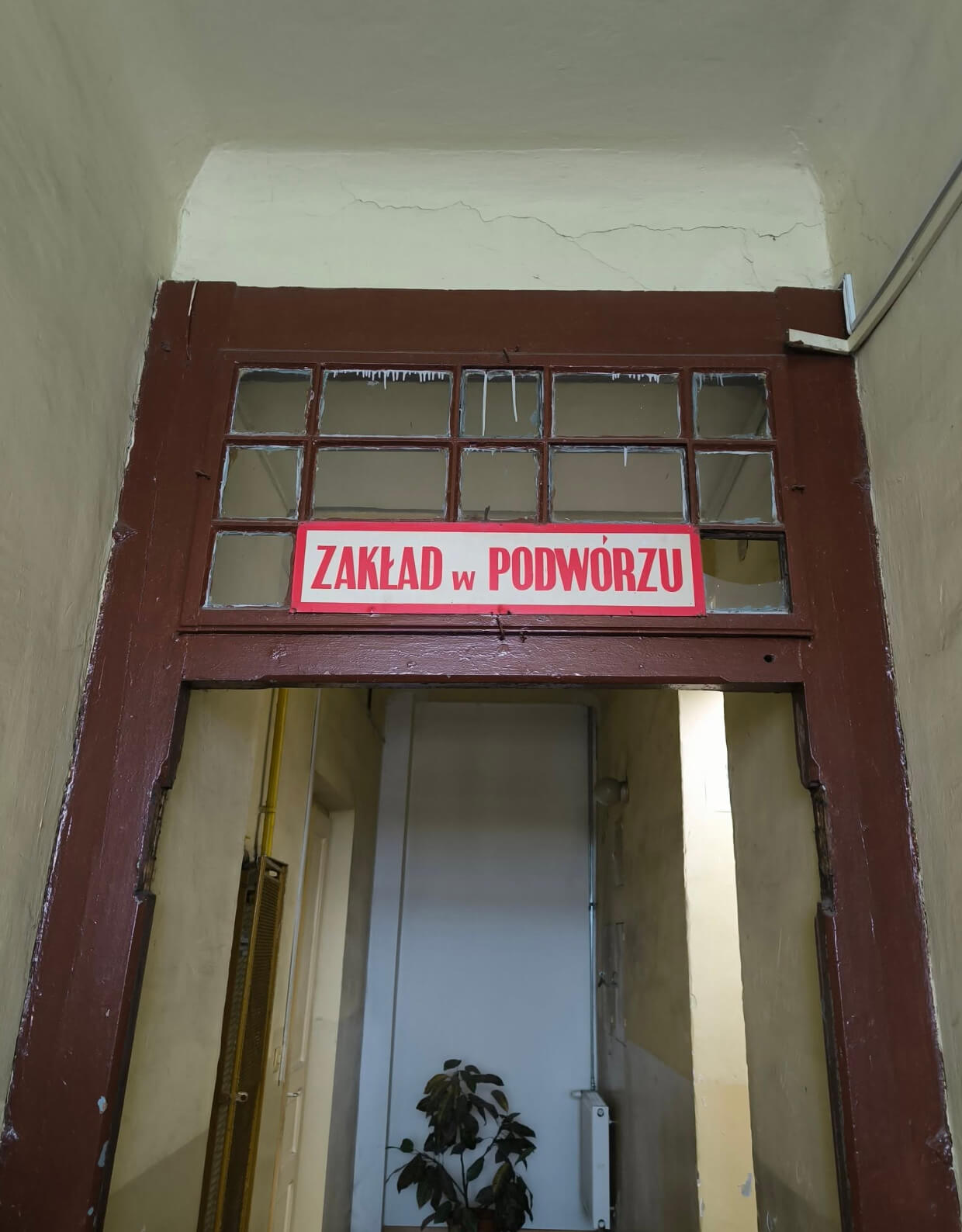 Przejście bramne z czerwoną tabliczką „Zakład w podwórzu” nad drzwiami