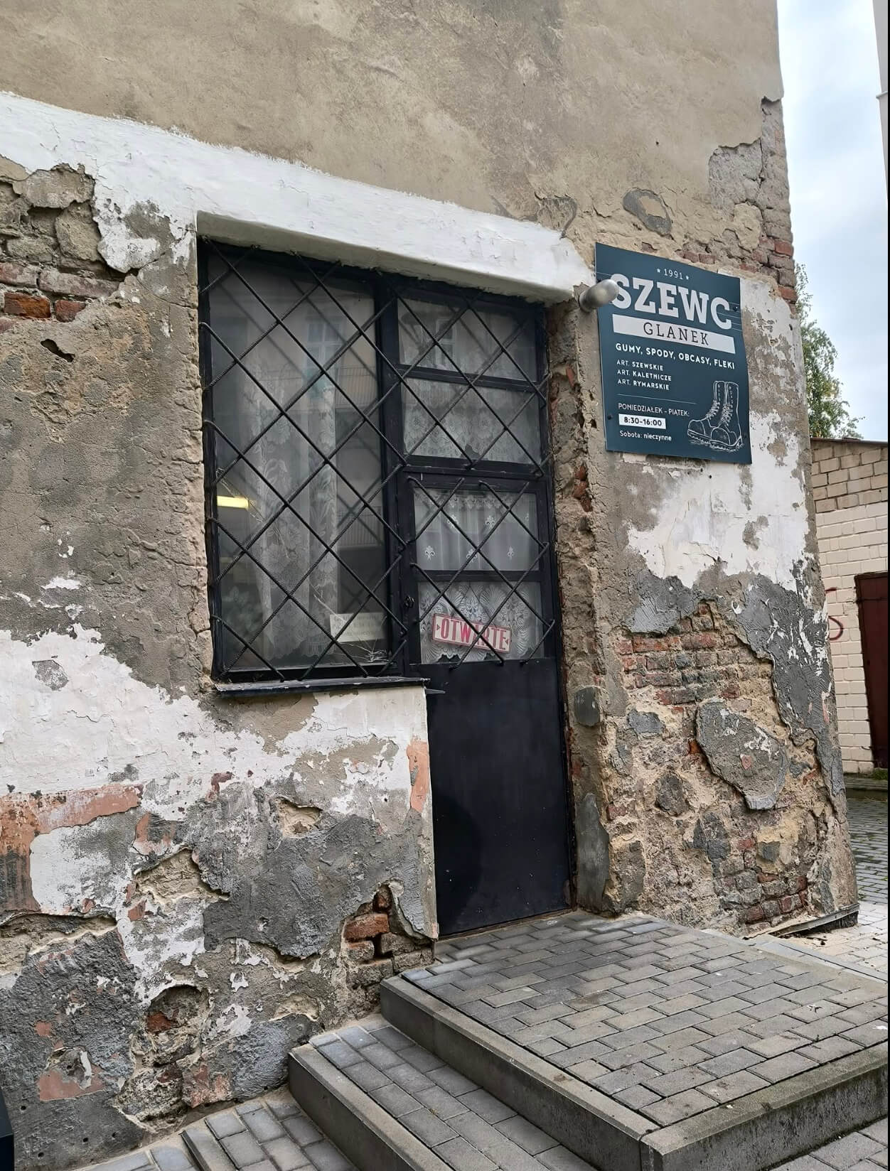 Wejście do zakładu szewskiego Glanek na podwórzu przy Sobieskiego 8 — ciemne drzwi z kartką „Otwarte” i szyld „Szewc Glanek, od 1991”